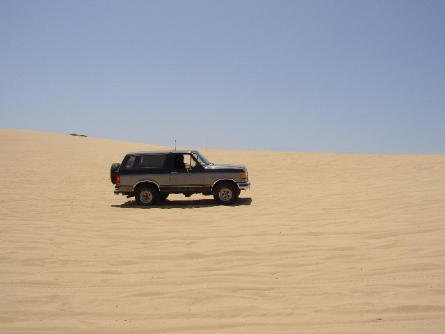 Two-tone silver and dark full-size Ford Bronco SUV parked side-on atop sand dunes
