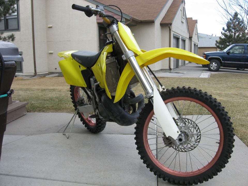 Yellow Suzuki dirt bike with red rims parked on driveway, front 3/4 view