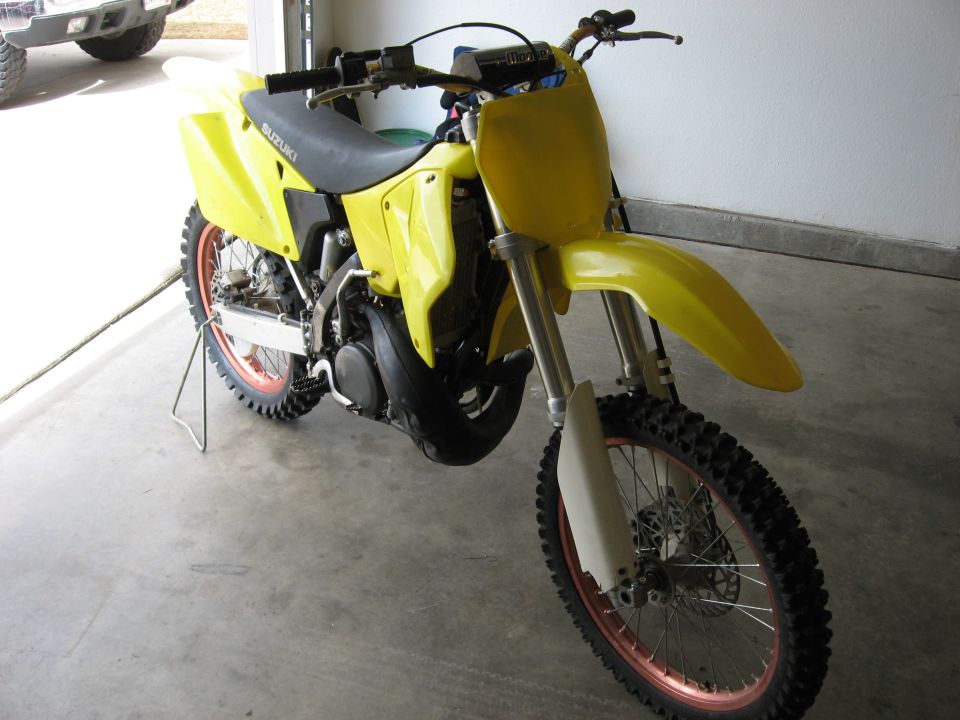 Yellow Suzuki dirt bike, front 3/4 view, red rims, in a garage
