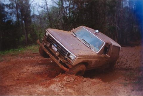 1984 Ford Bronco - This vehicle is stuck deep in the mud, with trees in the background.