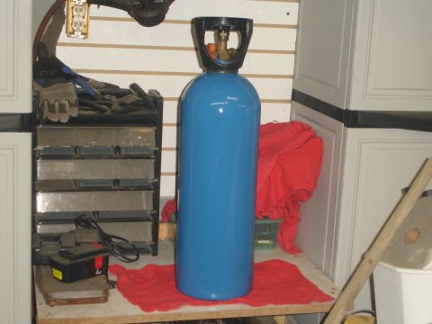 1989 Ford Bronco - A blue gas cylinder stands on a red cloth, with tools and cabinets in the background.