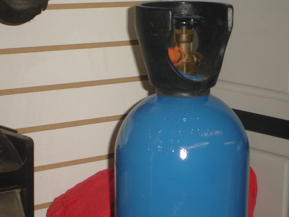 Blue gas cylinder with black valve assembly on top. Red cloth visible below