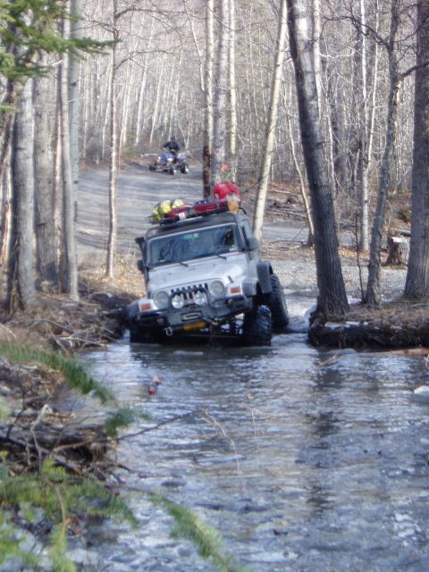 2000 Ford E350 - Jeep Wrangler navigating a stream on a wooded trail with an ATV in the distance.