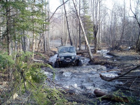 2000 Ford E350 - A Jeep Wrangler navigates a partially frozen stream surrounded by trees.