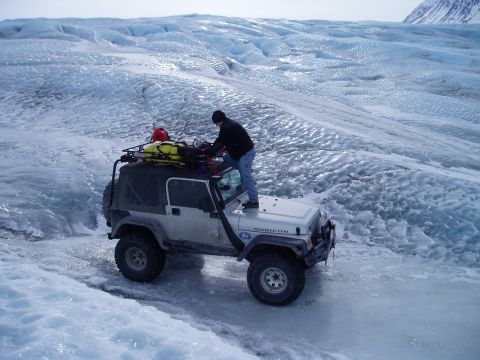 2000 Ford E350 - A Jeep Wrangler navigates an icy glacier, with a person securing equipment on its roof rack.