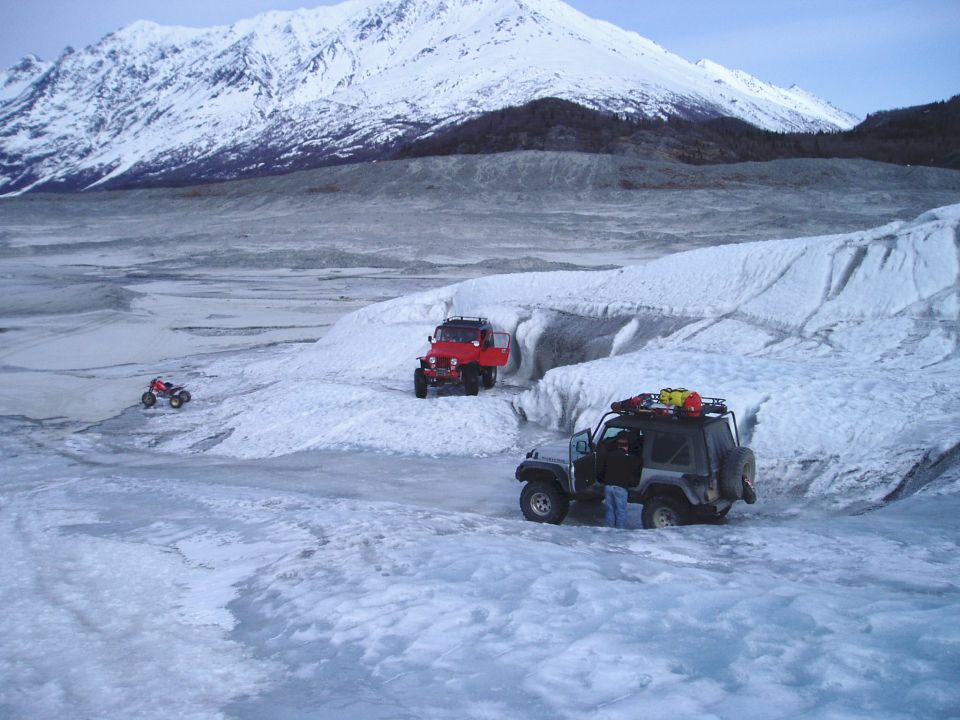 Silver Jeep Wrangler with roof rack on icy terrain, red Jeep CJ-7 behind