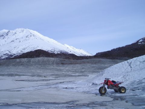 2000 Ford E350 - A red three-wheeled ATV sits on a frozen landscape with snow-capped mountains under a clear sky.