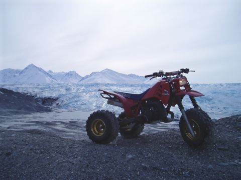 2000 Ford E350 - A red three-wheeled ATV sits in front of a vast glacier and mountain range under an overcast sky.