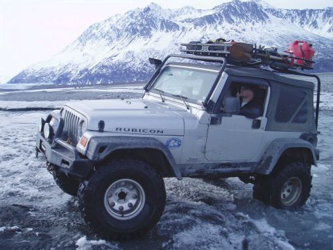 2000 Ford E350 - A Jeep Wrangler Rubicon navigates icy terrain with a snowy mountain range behind it.