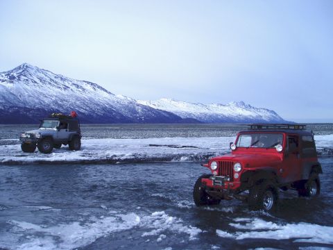 2000 Ford E350 - Two Jeeps navigate a partially frozen river with a snow-capped mountain range in the background.