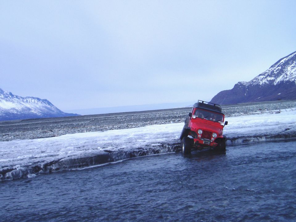 Red jeep driving through shallow water and ice with a roof rack