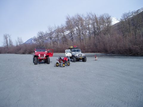 2000 Ford E350 - Two Jeeps and an ATV are parked on a wide, flat, gravelly area with trees and mountains in the background.