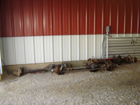 1992 Ford Bronco - Multiple vehicle axles are stored indoors on a gravel floor.