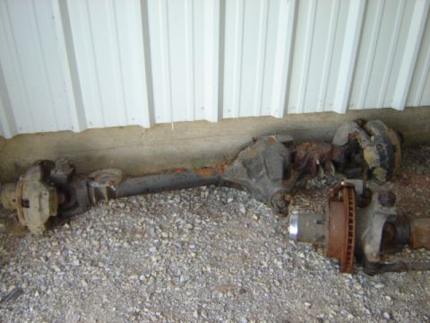 1992 Ford Bronco - Two vehicle axles, likely from a truck, are shown resting on a gravel surface.