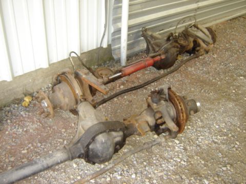 1992 Ford Bronco - Two vehicle axles, likely from a truck or SUV, are shown disassembled on a gravel surface.