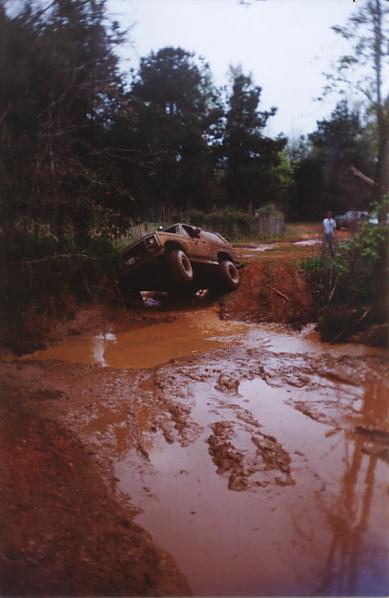1984 Ford Bronco - This vehicle is struggling to get through a challenging muddy terrain, with one side lifted high.
