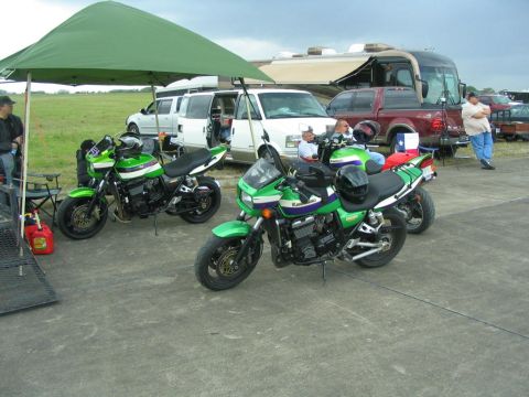 1981 Kawasaki Bayou - Several vehicles, including two green Kawasaki motorcycles, are parked outdoors under a cloudy sky.
