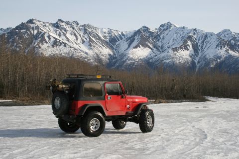2003 Jeep TJ - A red Jeep TJ sits on a frozen surface before snow-capped mountains.