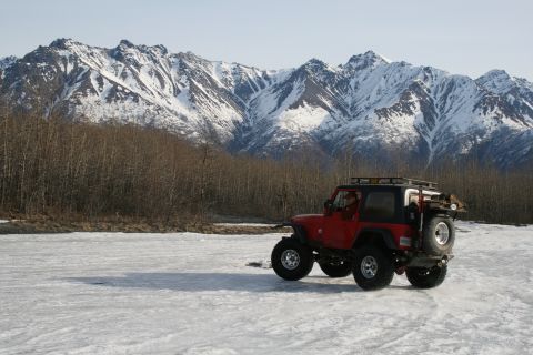 2003 Jeep TJ - A red 2003 Jeep TJ navigates an icy surface with snow-capped mountains in the background.