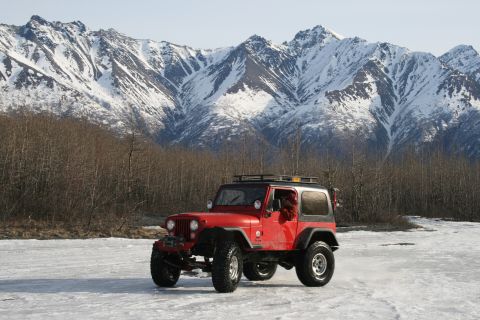2003 Jeep TJ - Red Jeep Wrangler parked on ice with snowy mountains behind it.