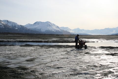 2003 Jeep TJ - A person stands with an ATV on a partially frozen landscape, with snow-capped mountains in the distance.