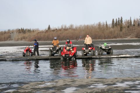 2003 Jeep TJ - A group of ATVs and their riders are gathered on a muddy and icy shoreline, with a line of trees visible in the distance.