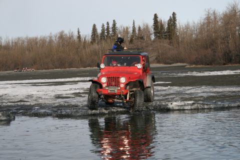 2003 Jeep TJ - A red Jeep Wrangler navigates a partially frozen body of water with trees in the background.