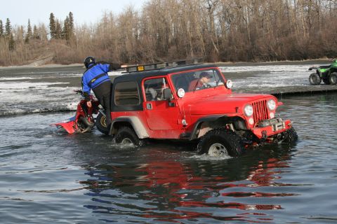 2003 Jeep TJ - A red 2003 Jeep TJ navigates through shallow water, with a jet ski attached to its rear.