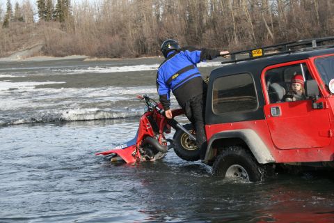 2003 Jeep TJ - A red ATV is partially submerged in water, with a person on it and a red Jeep nearby.