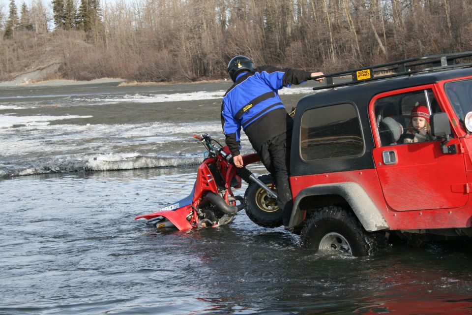 Red ATV stuck in water, with a person on it and a red Jeep next to it