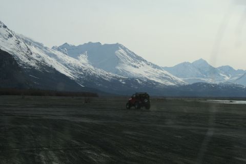 2003 Jeep TJ - A lone red off-road vehicle traverses a barren landscape with snow-capped mountains under a hazy sky.