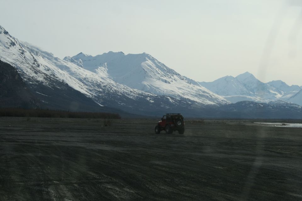 red off-road vehicle driving on a flat, dusty plain with snow-covered mountains in the background
