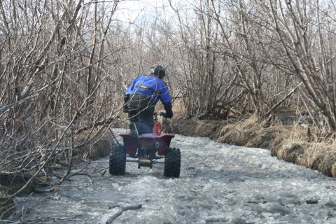 2003 Jeep TJ - Rider navigates an ATV through a partially frozen stream bed surrounded by leafless trees.