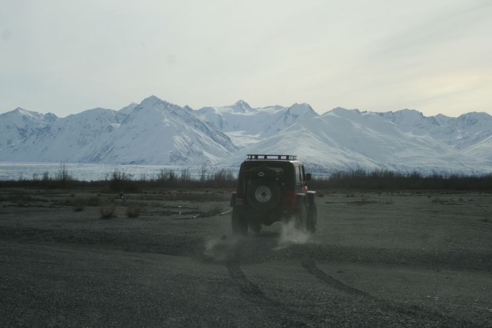 Red Jeep Wrangler driving on a gravelly plain with snow-capped mountains in the background