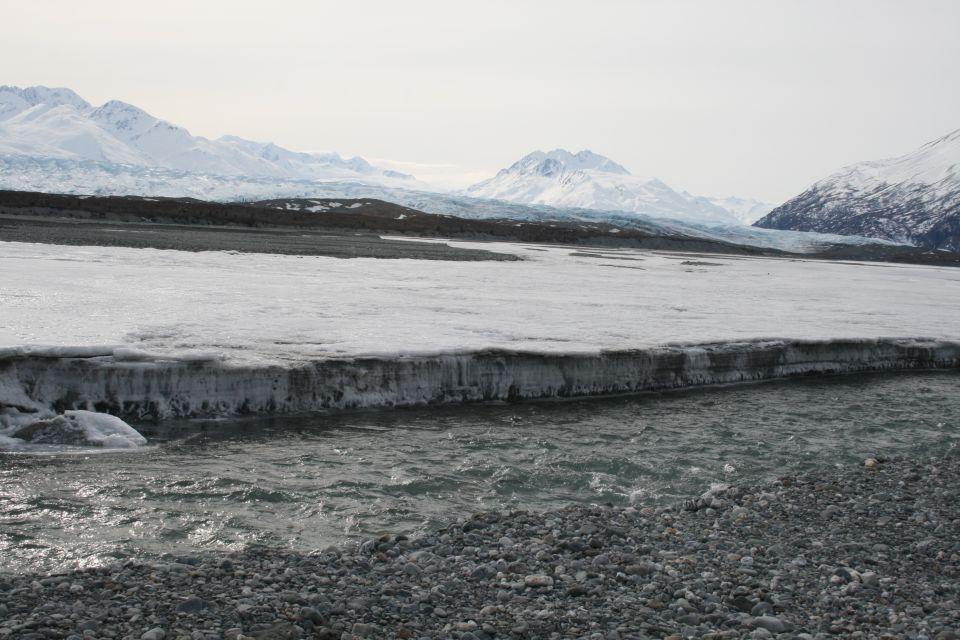 Frozen river with ice formations in foreground, snow-capped mountains and glacier in background