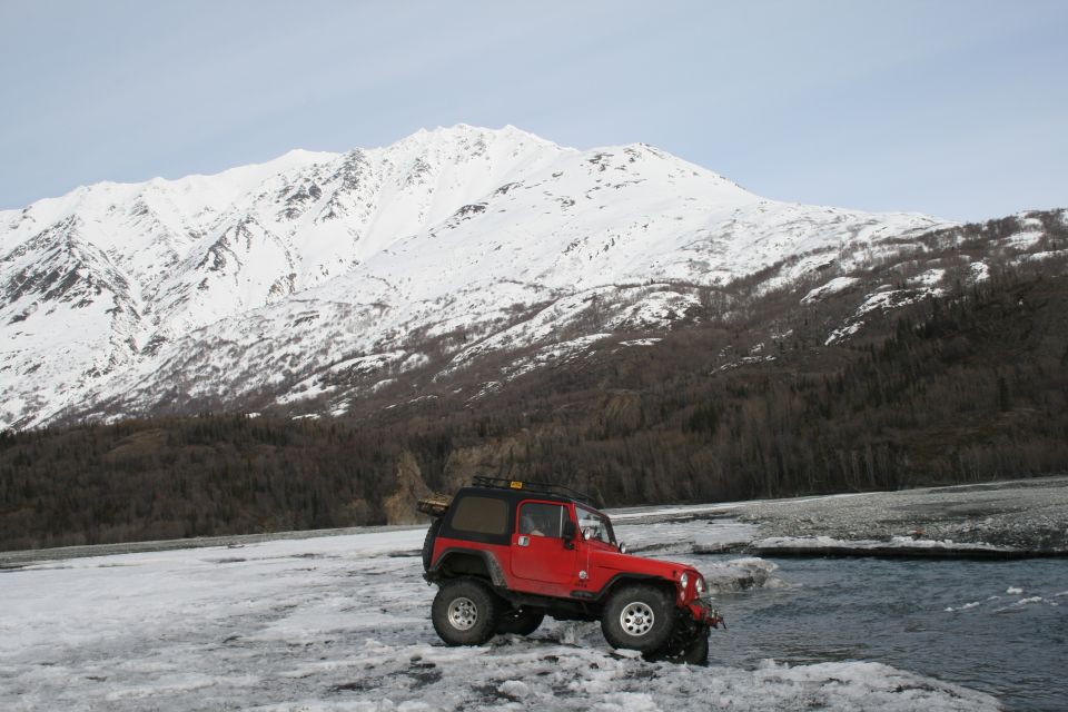 Red 2003 Jeep TJ parked on icy ground near a river with snow-covered mountains in the background