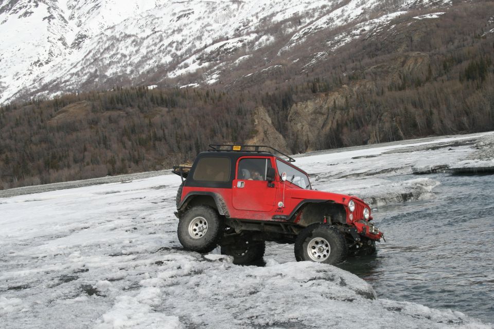 Red 2003 Jeep TJ on icy ground near water with snowy mountains behind