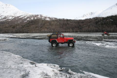 2003 Jeep TJ - A red Jeep Wrangler navigates a shallow, icy river with a red ATV in the distance.