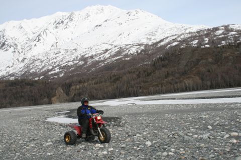 2003 Jeep TJ - A person rides a red three-wheeled ATV across a rocky, icy terrain with a large, snow-capped mountain in the background.