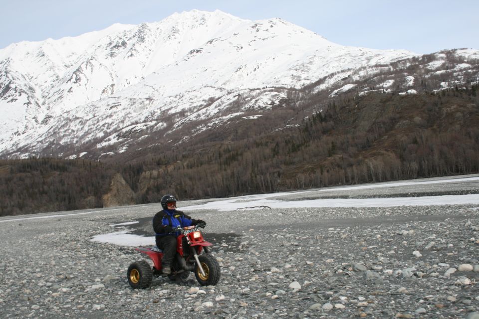 Red three-wheeled ATV with rider on a rocky, icy plain below a snow-covered mountain