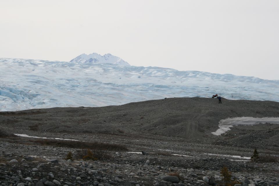 people on a rocky hill with a large glacier and snow-capped mountains behind them