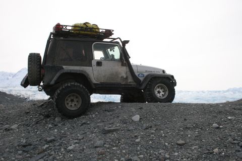 2003 Jeep TJ - A white 2003 Jeep TJ Rubicon with a roof rack and snorkel is parked on a rocky shore with a glacier in the background.