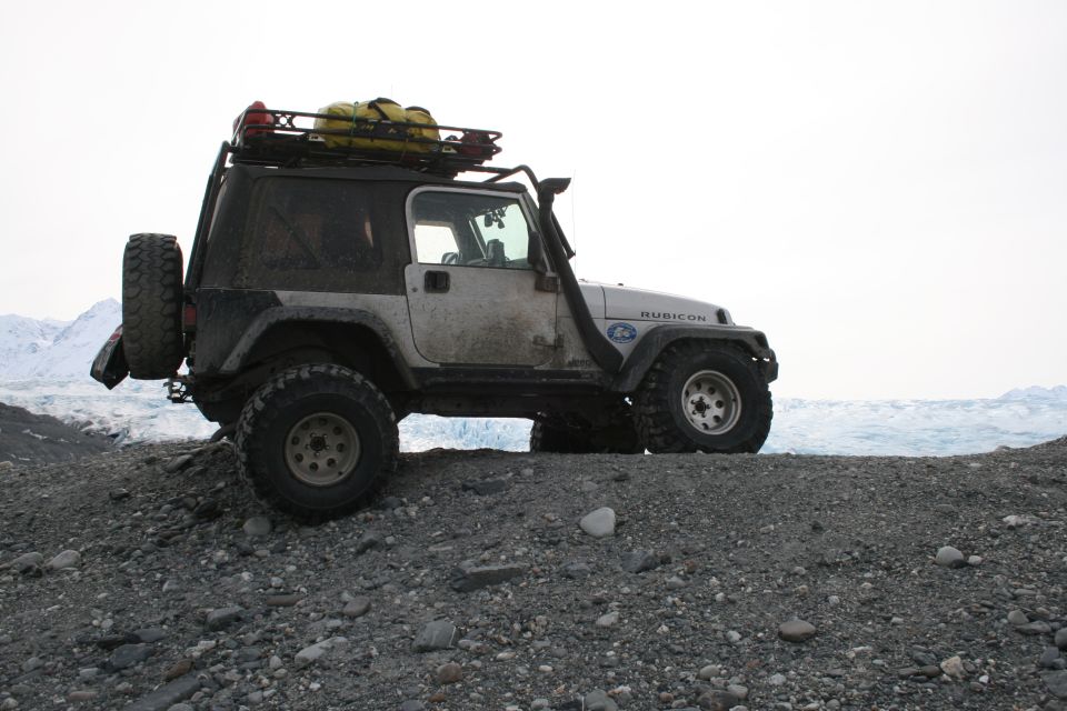 White 2003 Jeep TJ Rubicon with a roof rack and snorkel parked on a rocky shore