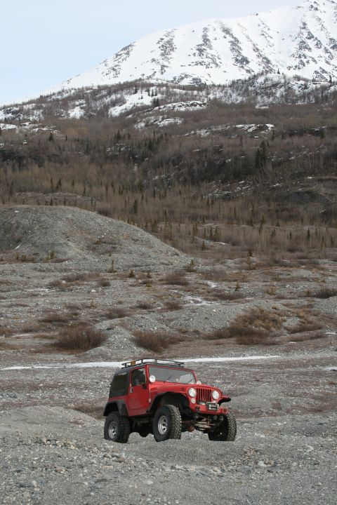2003 Jeep TJ - A red Jeep Wrangler is parked on a rocky, barren landscape with a snow-covered mountain in the distance.