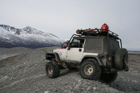 2003 Jeep TJ - A white Jeep Wrangler is parked on a rocky, desolate landscape with snow-covered mountains under a cloudy sky.