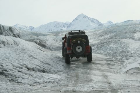 2003 Jeep TJ - A red 2003 Jeep TJ navigates a glistening icy path through a vast glacial landscape under a cloudy sky.