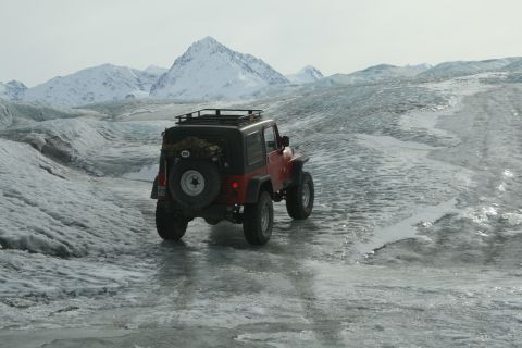 2003 Jeep TJ - A red 2003 Jeep TJ navigates a glacial landscape under a cloudy sky, with mountains in the background.