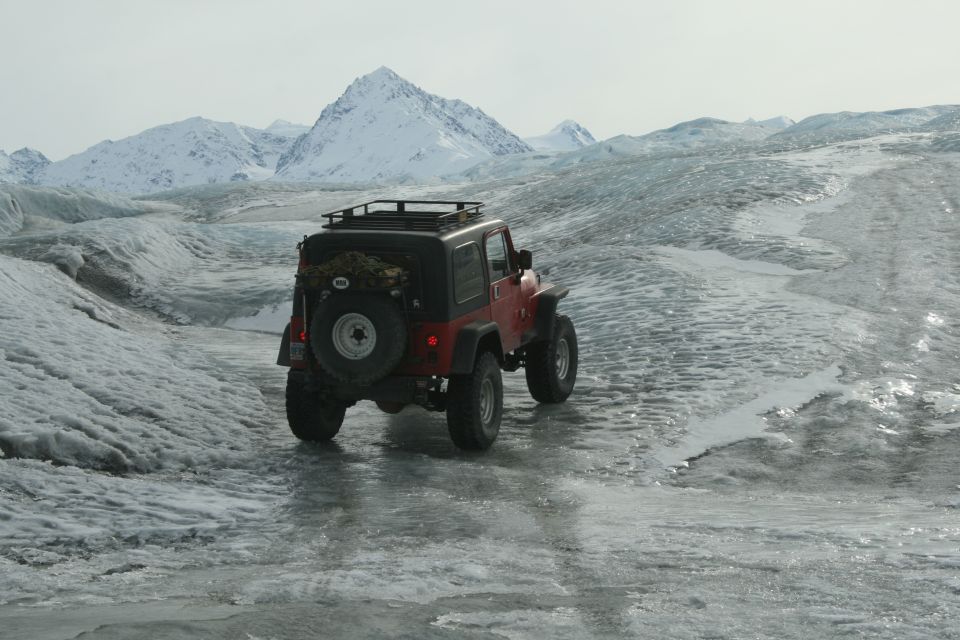 Red 2003 Jeep TJ on a glacier with snow-capped mountains