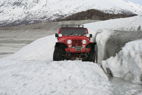2003 Jeep TJ - Red Jeep CJ navigates a snowy path near a glacier, with snow-covered mountains behind.