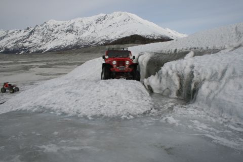 2003 Jeep TJ - A red Jeep navigates an icy terrain with a snow-capped mountain range in the background.